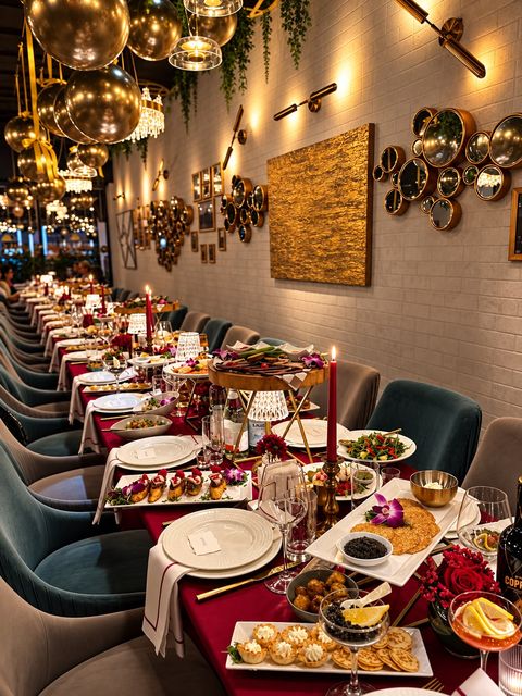 Banquet table set for a private event: burgundy tablecloth, red candles, black caviar, canapés and salads beside the wall of round gold mirrors