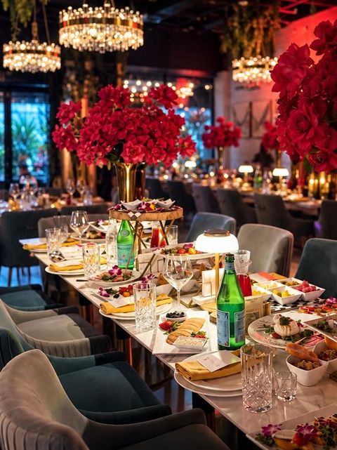 Baku Cafe's dining room at night: a long table set with small plates, red flower arrangements and crystal chandeliers